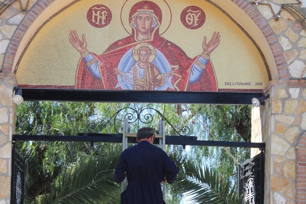 The priest is standing on a ladder to adorn the main entrance of the monastery with bay leaves. Bay leaves are the primary symbolic decoration of every religious place that celebrates.