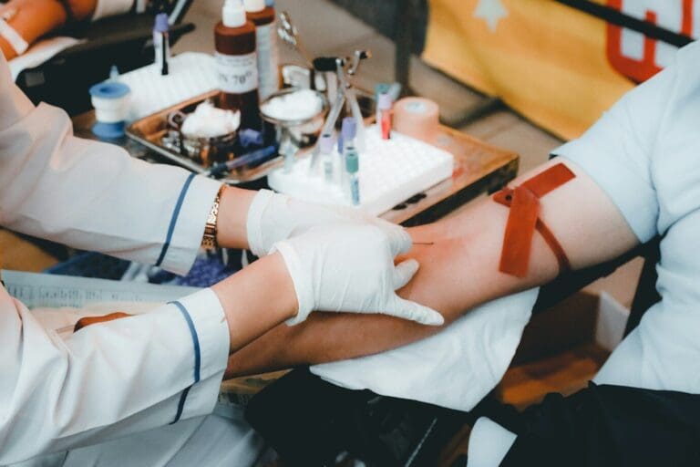 A healthcare worker in white gloves drawing blood from a person's arm